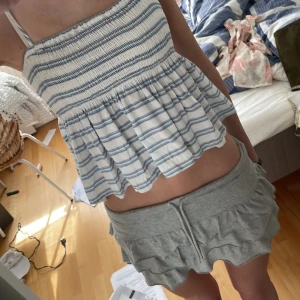 Randig linnetopp från Hollister - Supersöt vit och blå randig linnetopp från Hollister med volangig nederdel. Tunna axelband och luftig passform, perfekt för varma dagar. Snygg till både shorts, jeans och kjol. Storlek S, 