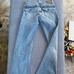 Blå bootcut jeans - Snygga blå bootcut jeans med klassisk femficksdesign och knappdetaljer på bakfickorna. Perfekta för en avslappnad stil. Från H&M slutsåld (tror jag). Pris kan alltid diskuteras, för mer info kontakta gärna mig (Obs bild på den kan skickas) 💕😊