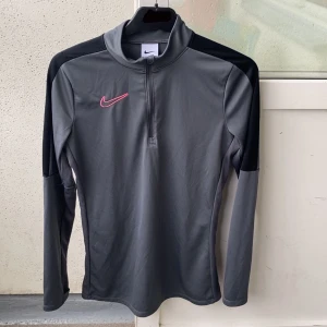 Nike dri-fit - Nike dri-fit academy grå med svarta detaljer på axlarna och rosa logga på bröstet. Inga tecken på användning. Tröjan har halv dragkedja framtill och Perfekt för träning eller sportaktiviteter. 💓