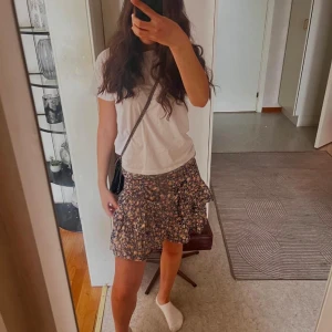 Blommig volangkjol  - Supersöt kort kjol med blommigt mönster i mörkblått, vitt och rosa. Kjolen har volangdetaljer och resår i midjan för en bekväm passform. Perfekt att styla med en enkel t-shirt eller blus.