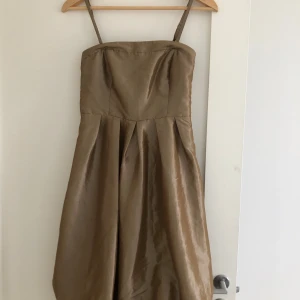 Champagnefärgad axelbandsklänning - Säljer en elegant champagnefärgad klänning med smala axelband och markerad midja. Klänningen har en lätt glansig yta och ballong kjol. 