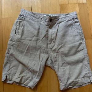 Beige linneshorts från Kappahl - Snygga beige shorts i linne från Kappahl med normal passform. Klassisk design med sidfickor, bakficka med knapp och gylf med knappstängning. Perfekta för varma dagar.