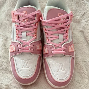 Louis Vuitton sneakers i rosa och vitt - Säljer ett par snygga Louis Vuitton sneakers i rosa och vitt. Skorna har tydliga LV-loggor, rosa snörning och detaljer samt vit bas. Perfekta för dig som vill sticka ut med exklusiva och trendiga sneakers.