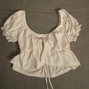 Vit croppad blus med puffärmar - Säljer en söt vit croppad blus med puffiga korta ärmar och knytning framtill. 