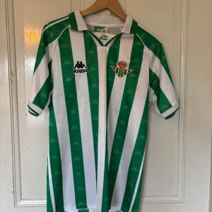 Real Betis fotbollströja  - Säljer en klassisk Real Betis fotbollströja från Kappa med gröna och vita vertikala ränder. Tröjan har klubbmärket på bröstet och Kappa-loggor i mönstret. Kortärmad och med krage, perfekt för fans av spansk fotboll.💯💯