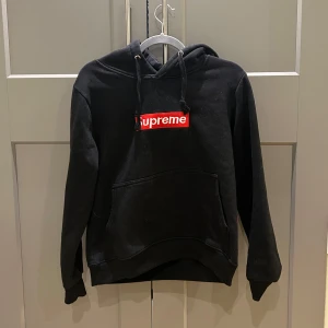Svart hoodie från Supreme - Säljer en svart hoodie från Supreme med klassisk röd box logo framtill. Tröjan har huva med dragsko och en stor magficka. Tillverkad i 100% bomull och har ribbade muddar vid ärmslut och nederkant.