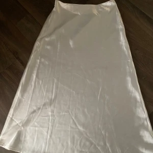 Vit satinkjol - Säljer en lång, vit kjol i satin med lätt glansig finish. Kjolen har en enkel och stilren design med lätt utställd form. Perfekt för dig som gillar minimalistisk stil och vill ha något som känns både trendigt och klassiskt.🤍