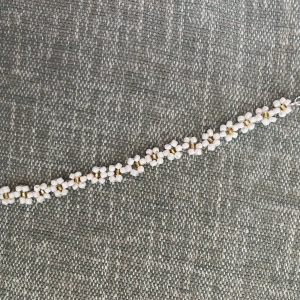 Pärlarmband med vita blommor - Sött armband med små vita pärlor formade som blommor och detaljer i guld. Justerbart spänne i silverfärg. 