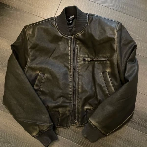 Skinnjacka bombermodell - Hej! Säljer nu min skinnjacka i bombermodell från H&M då den inte kommer till användning, aldrig använd utan enbart provad. Svart/grön i färgen och storlek XS. Jackan har även bredare axlar, nypris 599 säljes för 200:-