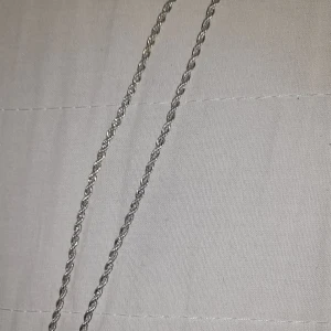 Silverfärgat tvinnat halsband - Säljer ett stilrent halsband i silverfärg med tvinnad kedja. Perfekt för dig som gillar enkla men snygga accessoarer. Passar till många olika stilar och är lätt att matcha med andra smycken.