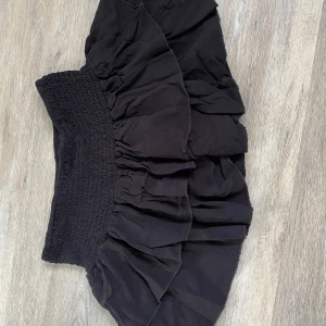 Kort svart volangkjol  - Supersöt svart kortkjol från SHEIN med bred smock i midjan och flera lager volanger. Perfekt för dig som gillar en feminin och trendig stil. Kjolen är lätt och luftig, vilket gör den enkel att matcha med olika toppar. Den är väldigt kort men kan fortfarande funka 