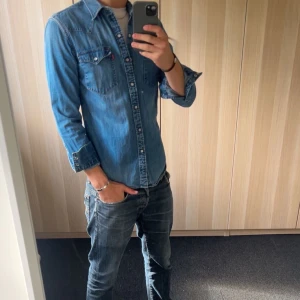 Jeansskjorta från Levi's - Säljer en vinted blå jeansskjorta från Levi's med långa ärmar och tryckknappar och en snygg western-inspirerad söm på ryggen. 