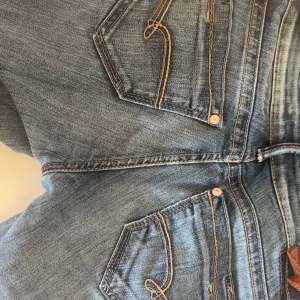 Blå lågmidjase jenas från Mari - Söta lågmidjade jeans med snygg ficka, köpta secondhand i Paris!! Används ett fåtal gånger och har hår som syns på sista bilden!! ( hålen syns inte när byxorna är på) skriv gärna privat för bilder och mått😊