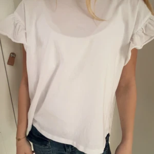 Vit blus med volangärmar - Säljer en vit blus med korta volangärmar. Blusen har en lös passform och är tillverkad i ett mjukt bomullstyg. Perfekt för en enkel och stilren look.