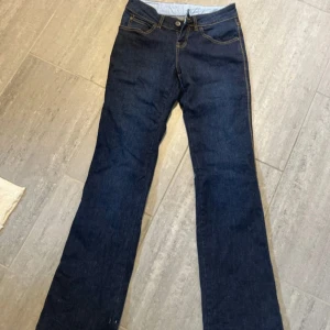Mörkblå bootcut jeans från Tatuum - Säljer ett par mörkblå bootcut jeans från Tatuum med klassiska gula sömmar och femficksmodell. Jeansen har normal passform och low/mide waist perfekta för en stilren look. Stängs med knapp och dragkedja.