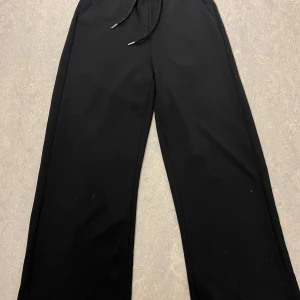 Svarta vida mjukisbyxor med dragsko low rise  - Svarta mjukisbyxor med breda ben och dragsko i midjan. Perfekta för en avslappnad stil och superbekväma att ha på sig. Passar till allt och är lätta att matcha med olika toppar.