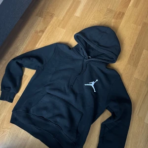 Jordan hoodie - Säljer en svart hoodie från Jordan med den ikoniska vita loggan på bröstet. Tröjan har en klassisk känguruficka och en bekväm huva med dragsko. 