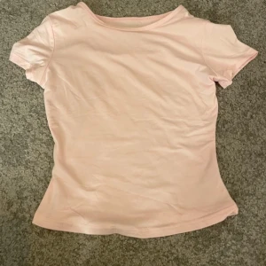 Ljusrosa t-shirt - Säljer en söt ljusrosa t-shirt med korta ärmar. Perfekt för en avslappnad stil. T-shirten är gjord i ett mjukt material som känns skönt mot huden. Aldrig använd! 