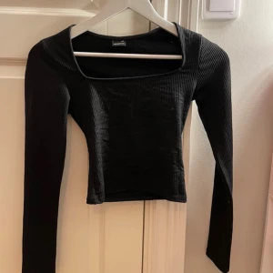 Svart ribbad topp - Snygg svart ribbad topp med långärmad design och fyrkantig halsringning. Perfekt för en stilren look. 