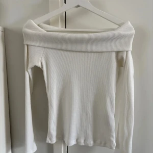 Vit ribbad offshoulder topp från Gina Tricot - Säljer en stilren vit ribbad offshoulder topp från Gina Tricot. Toppen har långa ärmar och en bred kant vid axlarna som ger en snygg look. Perfekt för att klä upp eller ner beroende på tillfälle. Passar bra till både jeans och kjol! Storlek S. Nyskick