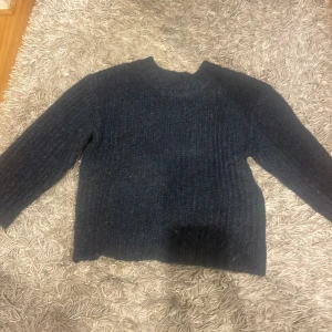Mörkblå stickad tröja från 157 - Säljer en mysig mörkblå stickad tröja från 157. Perfekt för kyliga dagar med sin varma och bekväma design. Tröjan är kort i ärmar och en klassisk rund halsringning. Passar utmärkt för både vardag och avslappnade tillfällen.
