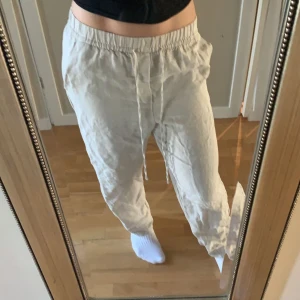 Beige linnebyxor med snörning - Säljer ett par bekväma beige linnebyxor med elastisk midja och snörning. Perfekta för en avslappnad stil. Byxorna har en loose passform och är tillverkade i ett lätt och luftigt material.