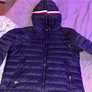 Mörkblå dunjacka från Moncler - Säljer en snygg mörkblå dunjacka från Moncler med huva och dragkedja. Jackan har ett stilrent randigt mönster i rött och vitt på huvan och Moncler-logga på ärmen. Perfekt för kyliga dagar! sitter som en s står ingen storlek❤️ priset går och diskutera 