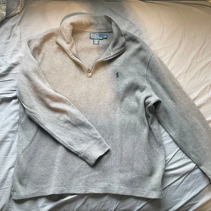 Grå tröja från Polo Ralph Lauren - Säljer en stilren grå tröja från Polo Ralph Lauren i storlek L. Tröjan har en halv dragkedja och är tillverkad i 100% bomull. Perfekt för en avslappnad look med sin klassiska design och långa ärmar. Nypris: 1900kr