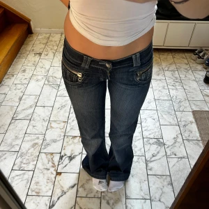 Y2k lågmidjade bootcut jeans - Snygga mörkblå bootcut jeans med unika fickdetaljer och dragkedja. Perfekta för en avslappnad stil med en touch av retro. De har en klassisk femficksdesign och är tillverkade i slitstarkt denim.
