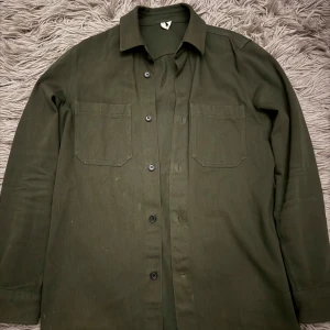 Olivgrön overshirt från Arket - Snygg olivgrön overshirt med knappar och två bröstfickor. Passar bra till både casual och mer uppklädda tillfällen. Passar även nu till våren. Bara att skriva vid minsta fundering!