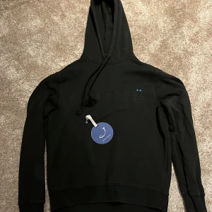 Svart hoodie från Jacob Cohën - Säljer en stilren svart hoodie från Jacob Cohën med broderad logga på bröstet. Den har en justerbar huva med snören och ribbade muddar vid ärmslut och nederkant. Perfekt för en avslappnad look. Storlek m men passar s