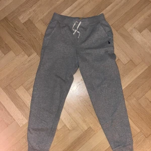 Grå mjukisbyxor från Polo Ralph Lauren storlek 14-16 år - Snygga grå mjukisbyxor från Polo Ralph Lauren med en liten broderad logga på sidan. Byxorna har storlek 14-16 år. De har en snörning i midjan och är tillverkade i mjukt material för extra komfort. Perfekta för en avslappnad stil.