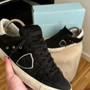 Svarta sneakers från Philippe Model - Snygga svarta sneakers från Philippe Model i nubuck med vita detaljer. Skorna har en klassisk design med snörning och en vit sula. Perfekta för en stilren look. Priset kan diskuteras vid en snabb affär