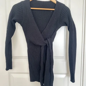 Svart ribbad kofta - Säljer en svart ribbad omlottkofta med knytband i midjan. Koftan är v-ringad och har långa ärmar, perfekt för kyligare dagar. Aldrig använd. 