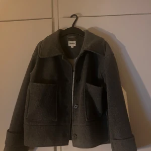 Grå kappa från Kappahl - Säljer en stilren grå kappa från Kappahl i storlek S. Jackan har en klassisk design med stora fickor och knappar framtill. Perfekt för kyligare dagar och ger en snygg look till din outfit.