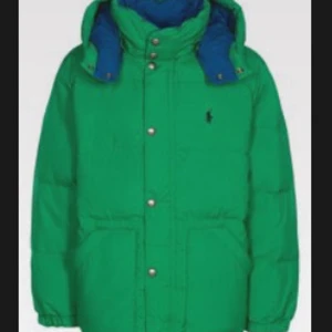 Grön dunjacka från Polo Ralph Lauren - Säljer en grön dunjacka från Polo Ralph Lauren med blå insida och huva. Jackan har knappar och dragkedja framtill samt två stora fickor.