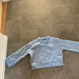 Ljusblå stickad tröja från Gina Tricot - Säljer en mysig ljusblå stickad tröja från Gina Tricot. Tröjan har en ribbad design och långa ärmar, perfekt för kyligare dagar. Den är både stilren och bekväm, idealisk för en avslappnad look. Passar perfekt till jeans eller kjol!