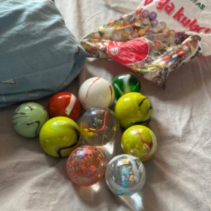 Påse med färgglada kulor från Tildas AB - En påse med färgglada kulor från Tildas AB. Kulorna har olika färger och mönster, inklusive röd, grön, gul och flerfärgade varianter. Perfekt för samlare eller lek. Påsen är märkt med 'Kuliga kulor!' och innehåller en blandning av olika kulor.