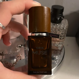 CAIA Muse Eau de Parfum - Säljer en elegant och stilren parfymflaska från CAIA med doften Muse. Flaskan är brun och fyrkantig med en matchande brun kork. Perfekt för den som söker en sofistikerad och modern doftupplevelse.