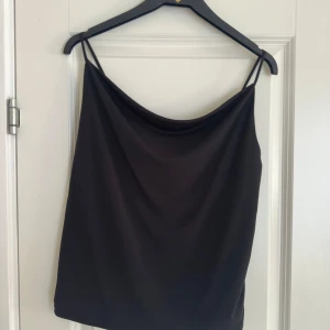 Svart topp med tunna axelband och drapering  - Snygg svart topp med smala axelband. Perfekt för en stilren look. Materialet är mjukt och följsamt.