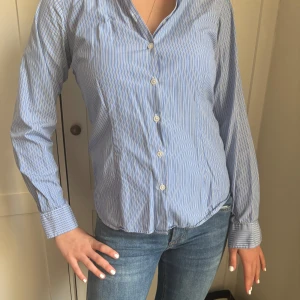Blå och vit randig skjorta från NewHouse - Snygg blå och vit randig bomullsskjorta med långa ärmar och knappar framtill. Skjortan har en klassisk vit krage som ger en stilren look. Perfekt för en chic och avslappnad stil. 