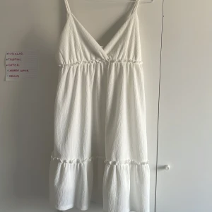 Vit klänning - Säljer en stilren vit klänning från H&M Divided. Klänningen har smala axelband och en v-ringad design. Perfekt för varma dagar med sin luftiga passform och lätta material.