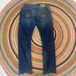 Blå jeansbyxor från Nudie Jeans - Snygga blå jeansbyxor från Nudie Jeans med klassisk femficksdesign och slitna detaljer. Byxorna har en rak passform och är tillverkade i bomull. Perfekta för en avslappnad stil. Storlek är 30/34 men sitter som 30/32.