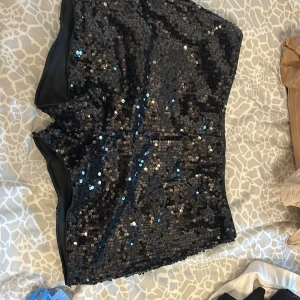 Svarta paljettshorts - Snygga svarta shorts täckta med glittrande paljetter. Perfekta för en festlig kväll när du vill sticka ut. De har en bekväm passform och är ett måste för garderoben om du älskar att glittra.