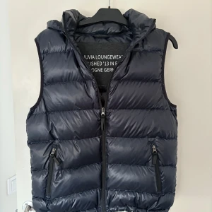 Mörkblå dunväst med huva - Snygg mörkblå dunväst med dragkedja och huva. Perfekt för våren. Den är näst intill ny, knappt än vänd.