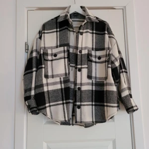 Svartvit rutig overshirt - Snygg och trendig svartvit rutig overshirt med knappar. Perfekt för lager-på-lager-stilen. Den har två stora bröstfickor och en avslappnad passform. Ett måste för garderoben!