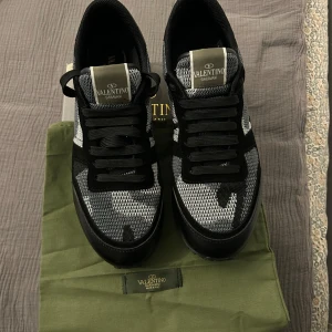 Valentino Rockrunners - Snygga Valentino Garavani sneakers i svart och grått med ett coolt camouflage-mönster. Skorna har snörning och en robust sula för extra grepp. Perfekta för att ge din outfit en stilfull touch. Lyxa till din vardag med ett par stilrena Valentino Rockrunners för endast 1949kr‼️  Tyvärr säljer jag de då de är för små för mig. Och känner att jag vill spara för ett par andra skor.  Storlek:43 Priset är ej hugget då priset kan gå ner vid snabb affär.  Dustbag samt annat utrustning kommer vid köpet!