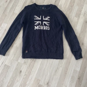  stickad tröja från Morris - Säljer en snygg svart stickad tröja från Morris med Union Jack-motiv och texten 'Morris' på framsidan. Perfekt inför våren och för en stilren look! Skick 8/10