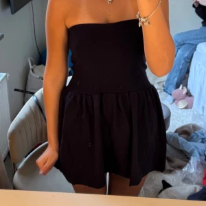 Svart axelbandslös kortklänning - Säljer en svart axelbandslös kortklänning med utställd kjol. Enkel och stilren design som passar perfekt när du vill känna dig extra fin. Klänningen har en feminin siluett och är lätt att matcha med smycken.