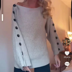 Beige stickad tröja med knappar på ärmarna - Säljer en beige stickad tröja med långa ärmar och svarta knappar längs hela ärmarna. Tröjan har en bred, rund halsringning och en avslappnad passform. Perfekt för lager-på-lager och enkel att styla till jeans eller leggings. SÅÅÅÅ SNYGG!!❤️❤️